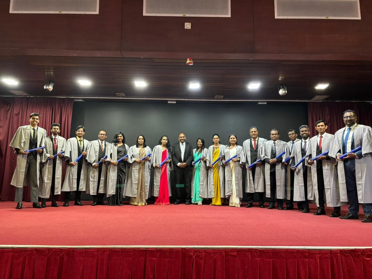 SLITAD graduates in gowns holding their certificates on stage